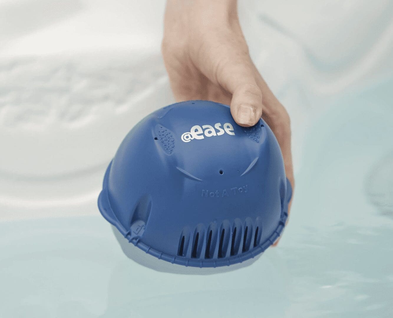 A person is holding a FROG @Ease Floating Sanitizing System for Hot Tubs in the water.